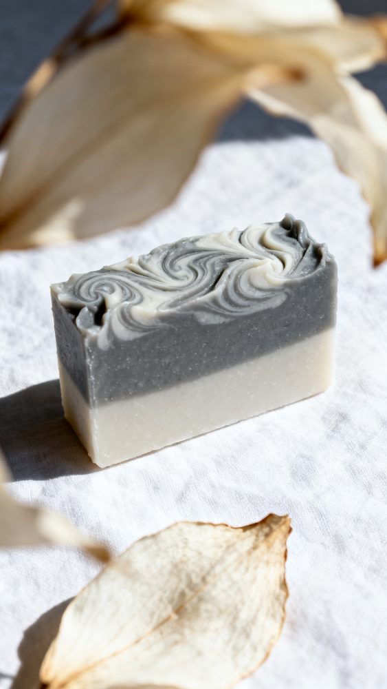Sabonete artesanal bicolor com textura ondulada em tecido branco com folhas secas ao redor