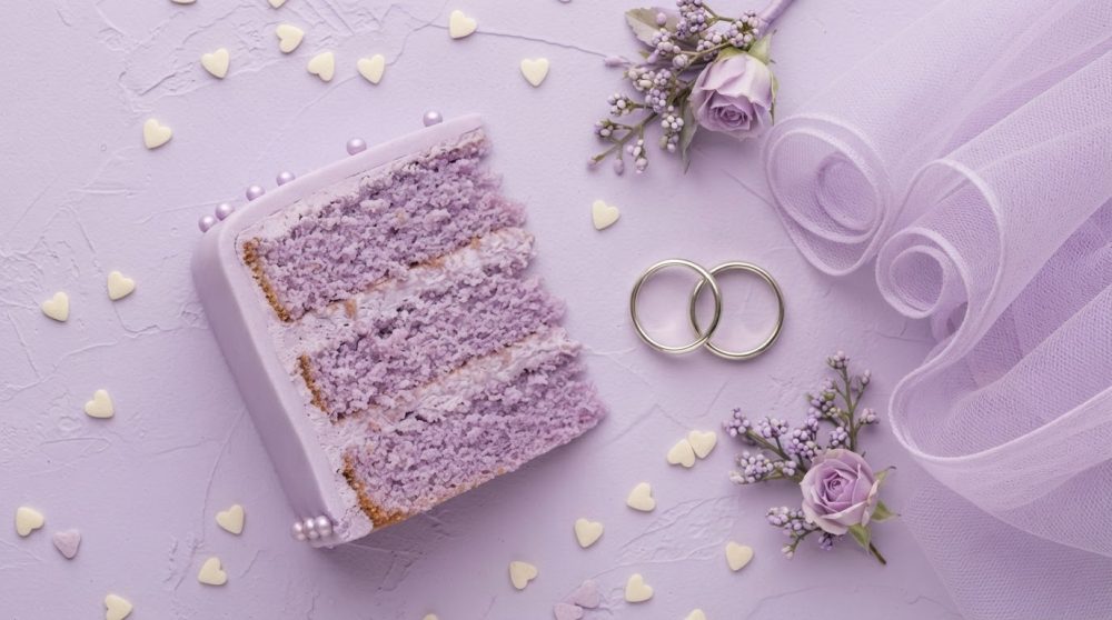 Fatia de bolo lilás com pérolas, alianças, flores e tecido translúcido para casamento