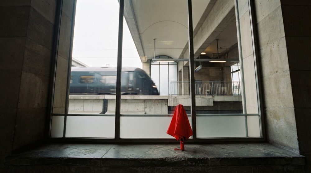 Comboio moderno em movimento na estação vista através de uma janela com guarda-chuva vermelho fechado no peitoril