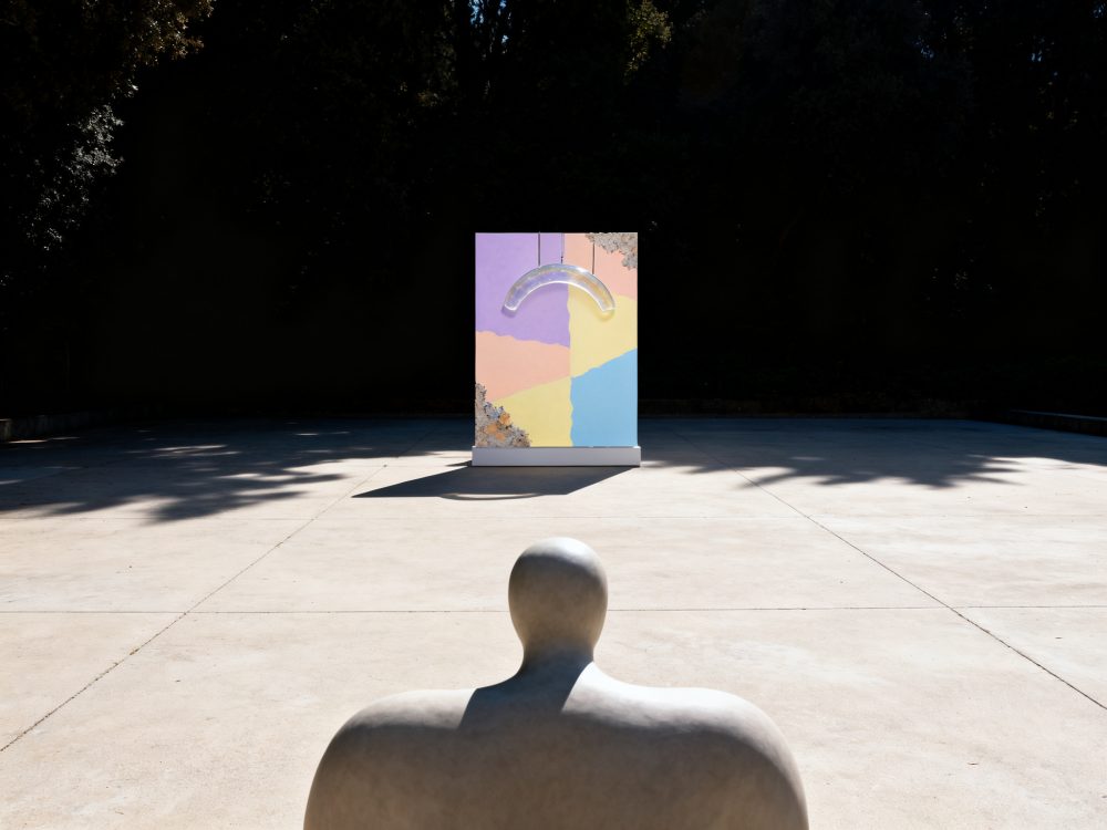 Escultura abstrata cinzenta com painel colorido em espaço exterior iluminado