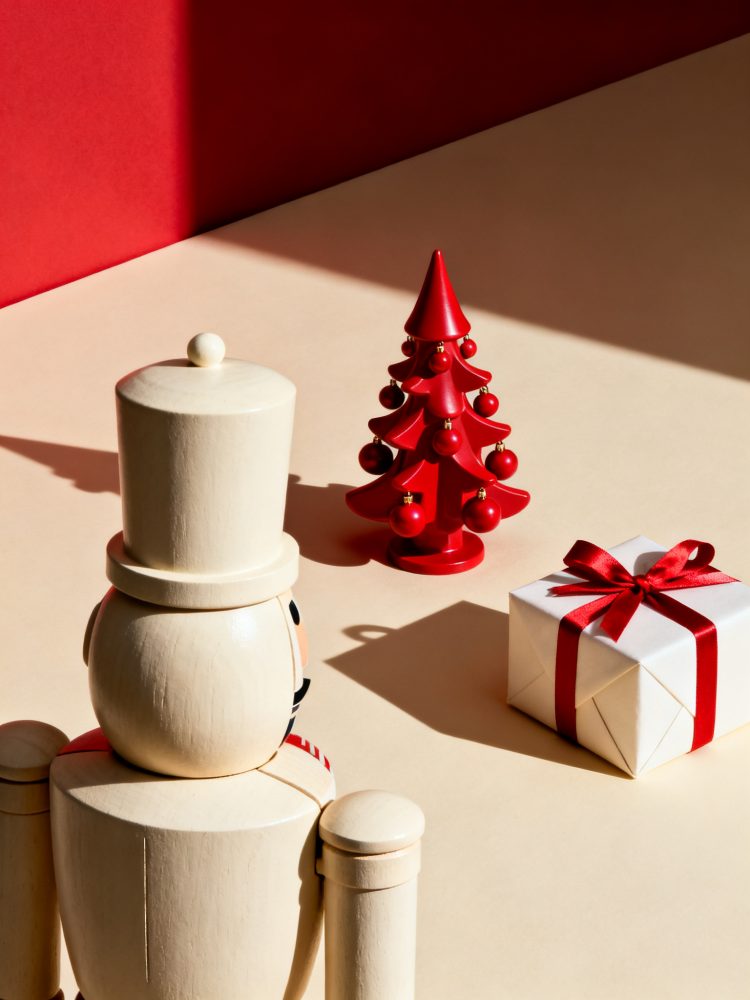 Nutcracker branco de madeira, pequena árvore de Natal vermelha e presente com laço vermelho sobre fundo claro e parede vermelha