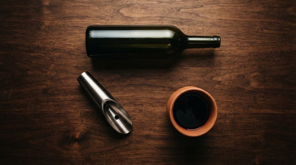 Garrafa de vinho, anel de aço inox e copo de vinho tinto sobre mesa de madeira escura