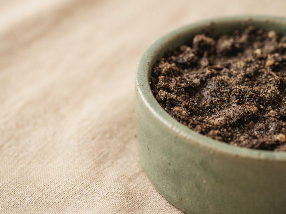 Vaso verde com terra húmida sobre tecido bege para jardinagem