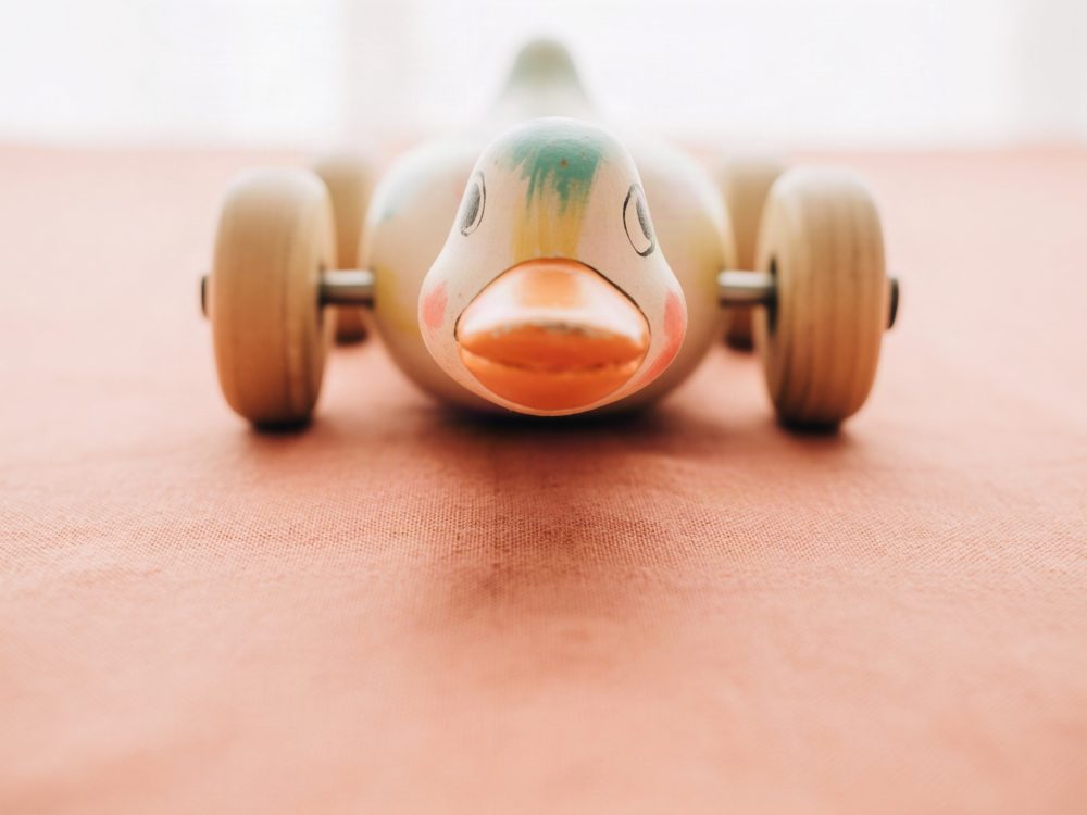 Brinquedo em madeira em forma de pato com rodas sobre tecido laranja