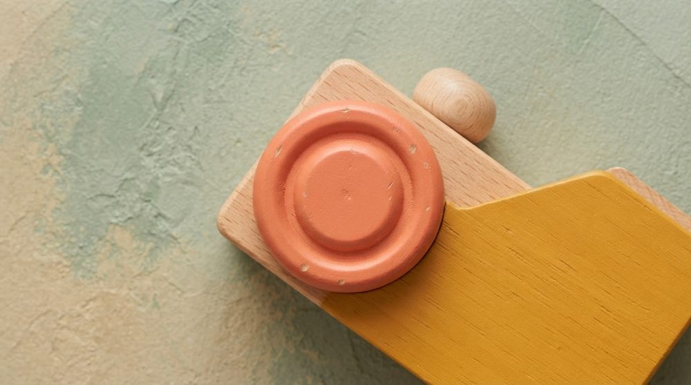Brinquedo de madeira pintado com amarelo e terracota sobre fundo texturado neutro