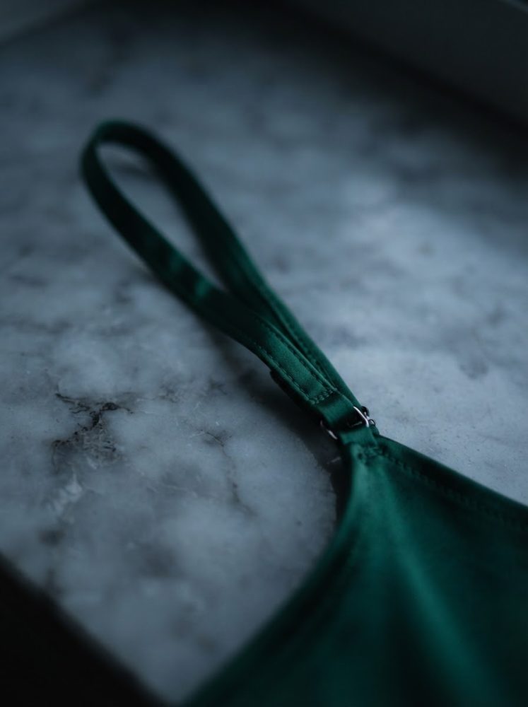Vista detalhada de alça verde de lingerie sobre superfície de mármore cinzenta