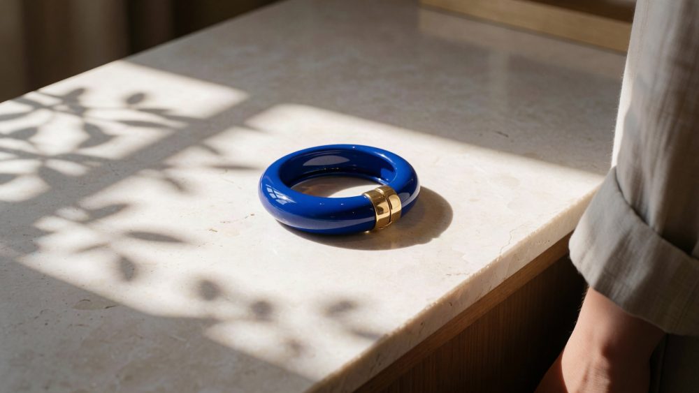 Pulseira azul royal com fecho dourado sobre superfície clara com sombras de plantas