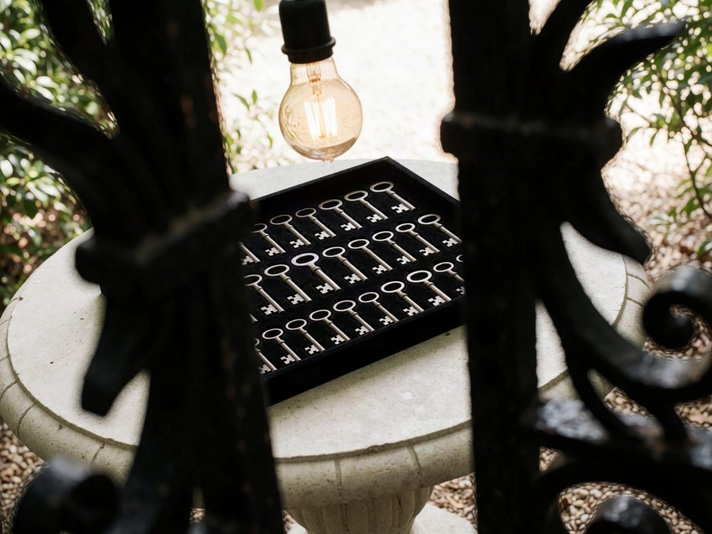 Chaves antigas organizadas num tabuleiro preto sobre mesa de pedra, luz de lâmpada amarela e grades de ferro em primeiro plano