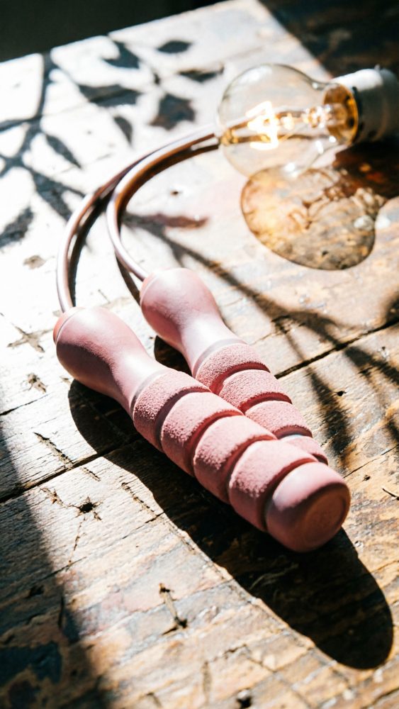 Corda de saltar rosa com pegas almofadadas numa mesa de madeira iluminada por luz natural