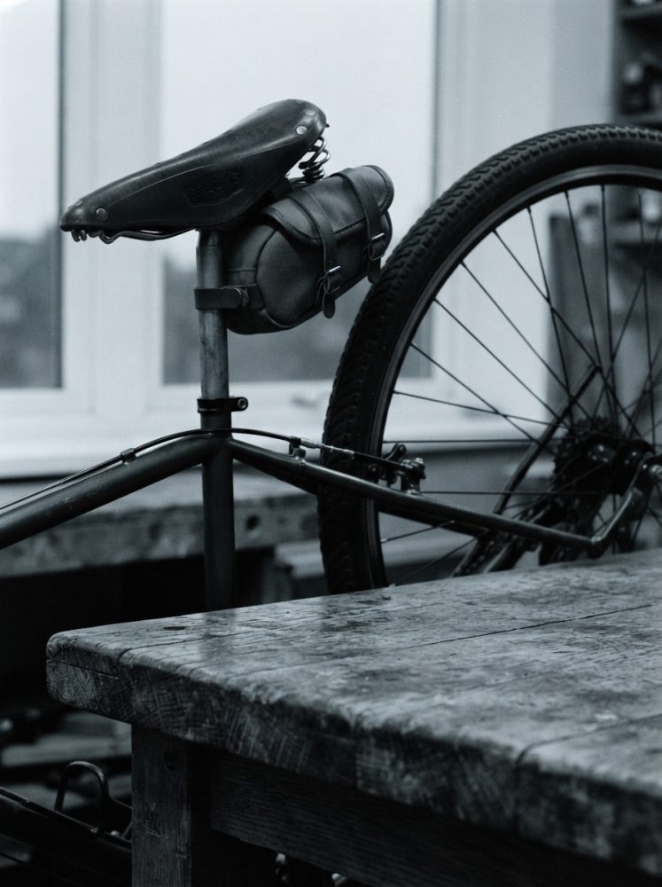 Parte traseira de bicicleta clássica com selim de couro e bolsa de armazenamento junto a mesa de madeira