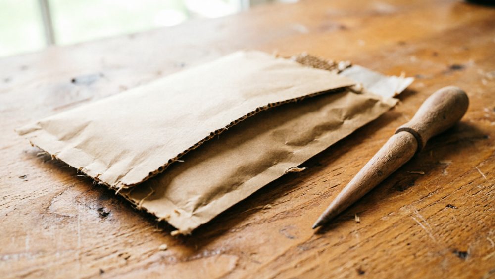 Envelope de papel kraft e ferramenta de punção de madeira sobre mesa de madeira