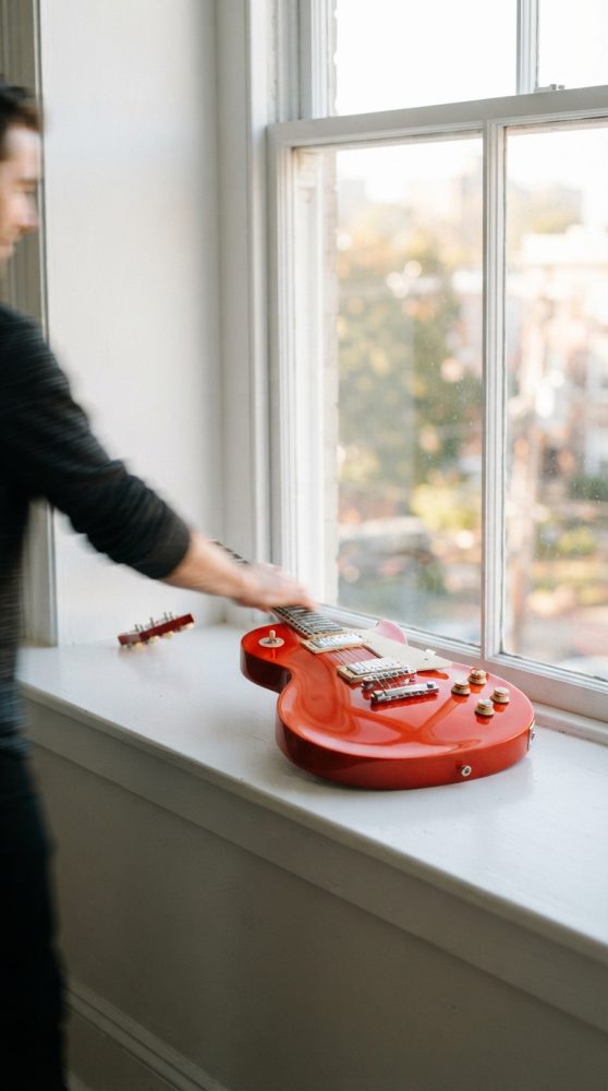 Guitarra elétrica vermelha sobre parapeito iluminada por luz natural ao lado de janela