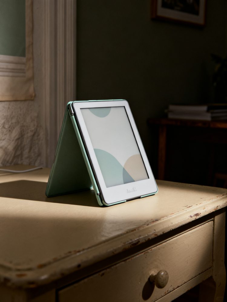 Leitor de e-books com capa verde aberto sobre mesa vintage de madeira clara iluminada por luz natural