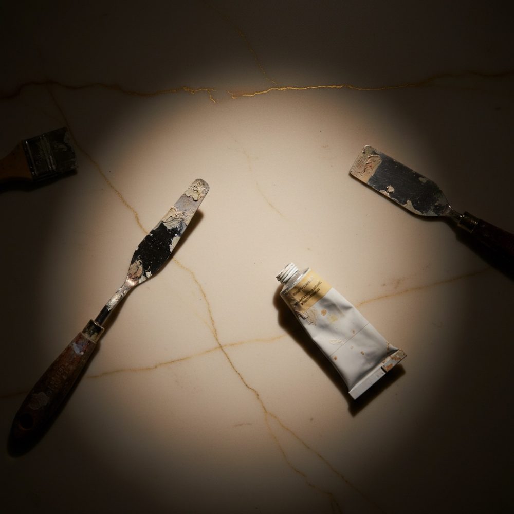 Espátulas com tinta e tubo de tinta sobre superfície de mármore bege com veios dourados