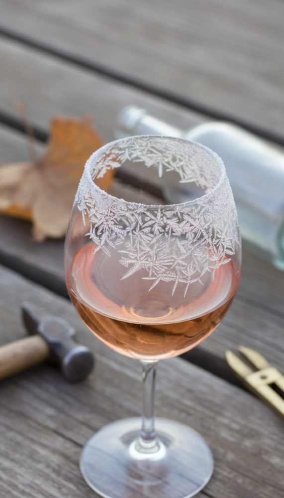 Taça de vinho rosé com borda de gelo decorativo sobre mesa de madeira com ferramentas e folha seca