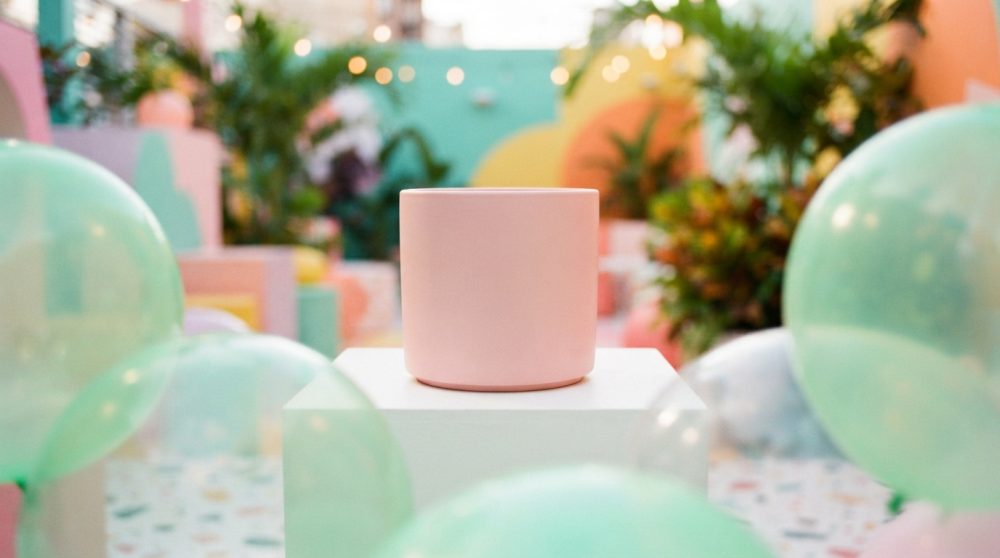 Copo rosa em suporte branco com balões verdes e fundo colorido desfocado