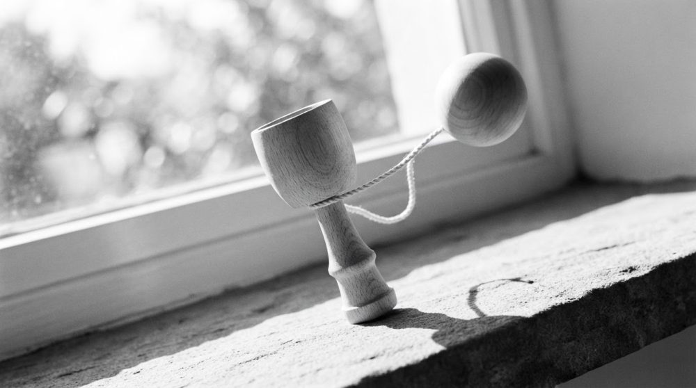 Kendama de madeira natural sobre peitoril de janela com sombra pronunciada
