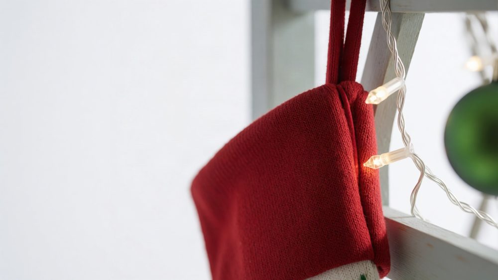 Meia vermelha de Natal pendurada numa estrutura branca com luzes amarelas e ornamento verde ao fundo