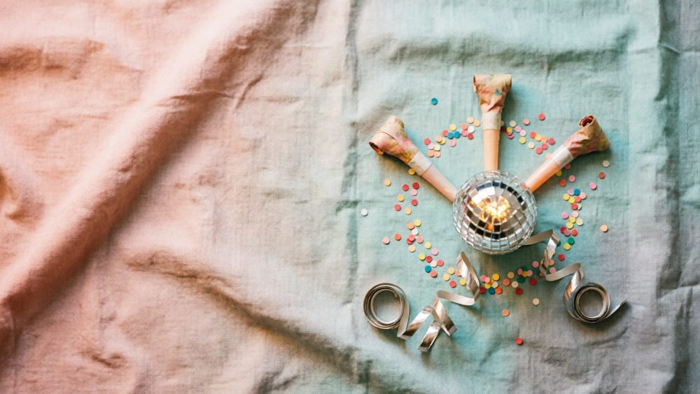 Acessórios coloridos de festa com apitos, serpentinas, confetis e bola de espelhos sobre tecido