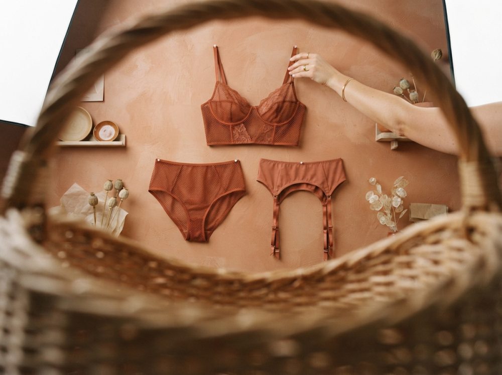 Conjunto de lingerie castanho com sutiã, cuecas e cinta-liga pendurado numa parede decorada