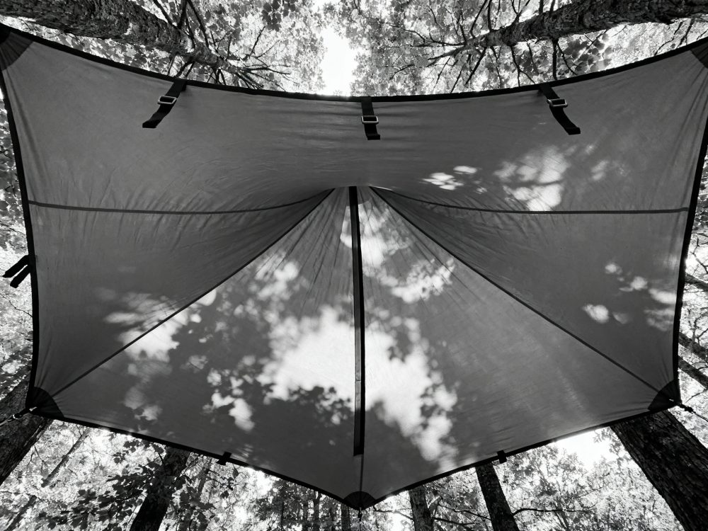 Toldo de camping suspenso entre árvores numa floresta com luz filtrada através das folhas