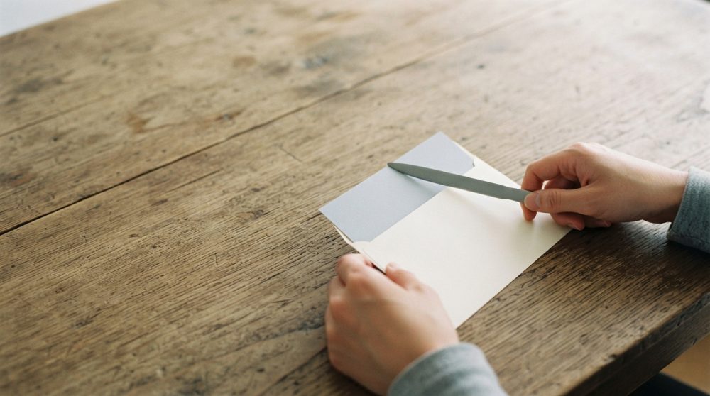 Mãos a segurar envelope branco sobre mesa de madeira rústica com luz suave