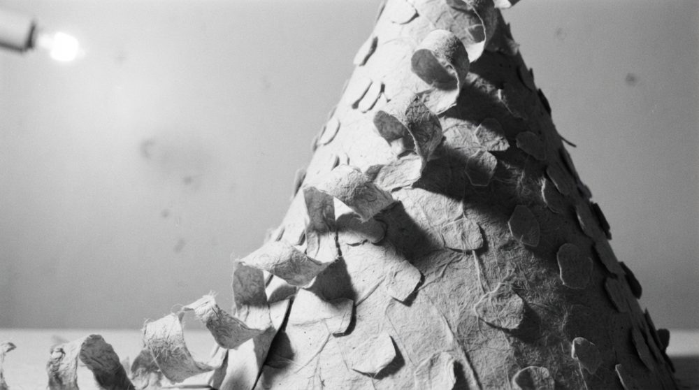 Chapéu cónico de festa feito de papel com textura e sombras marcadas em fundo neutro
