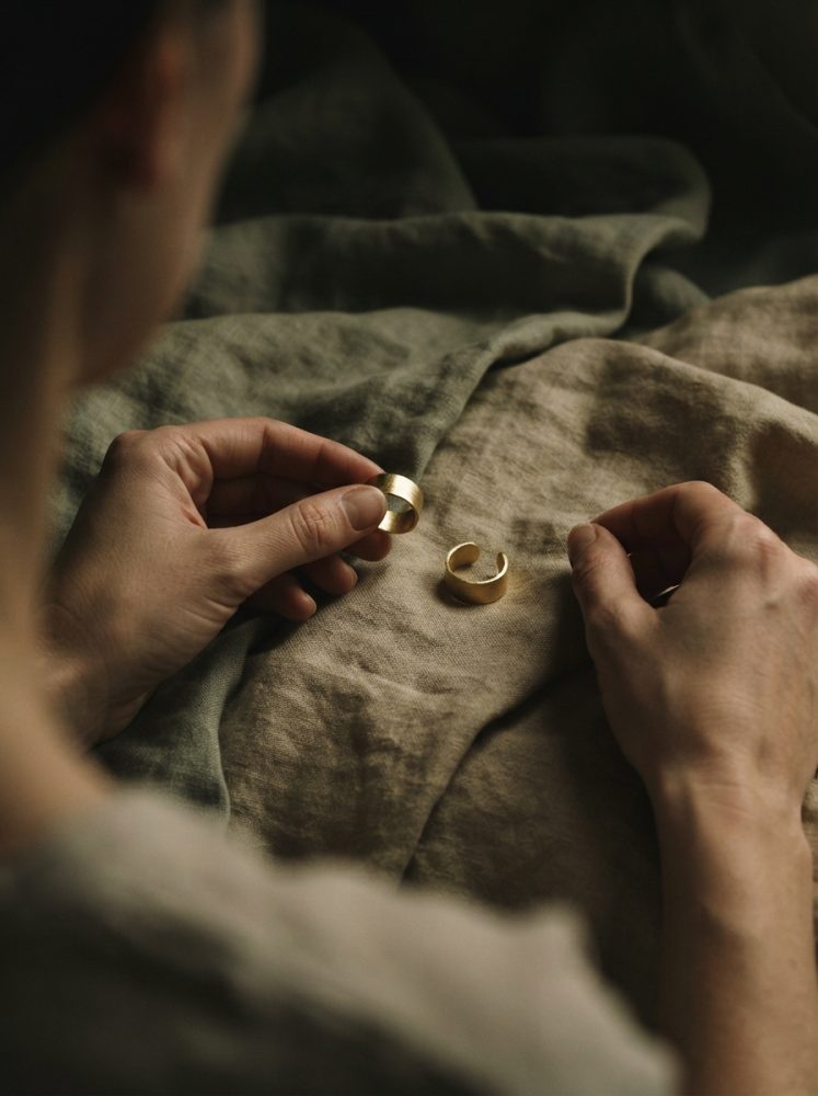 Mãos femininas seguram anéis dourados sobre tecido natural em tons terrosos
