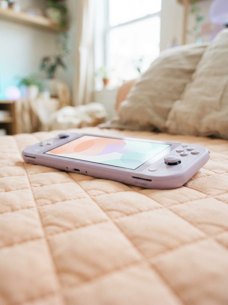 Console portátil lilás sobre colcha acolchoada bege numa cama com almofadas ao fundo