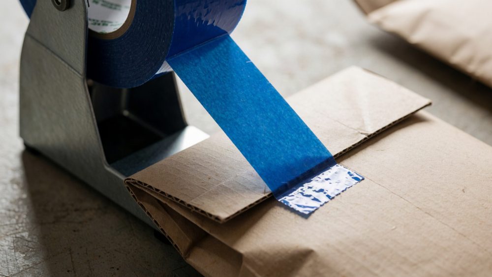 Fita adesiva azul num dispensador metálico a selar embrulho de papel kraft