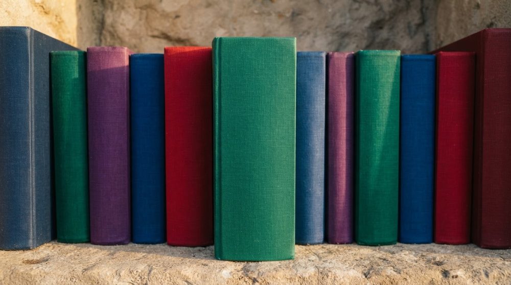 Livros de capa dura colorida alinhados sobre uma superfície de pedra rústica