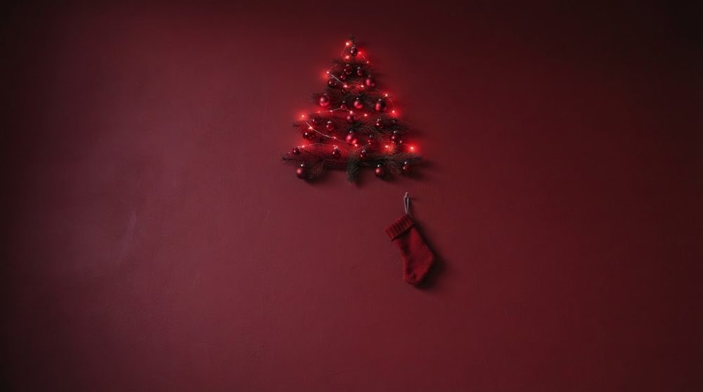 Árvore de Natal com luzes e bolas vermelhas sobre fundo bordô, com meia de malha pendurada