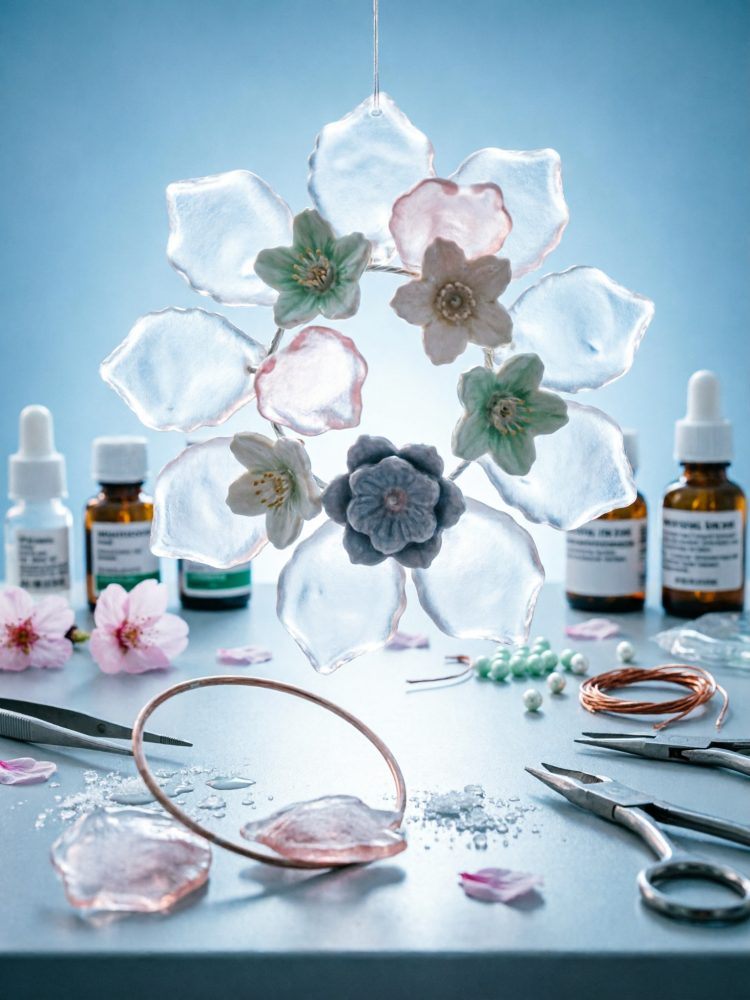 Móbile de flores em resina translúcida suspenso sobre bancada azul com ferramentas de artesanato