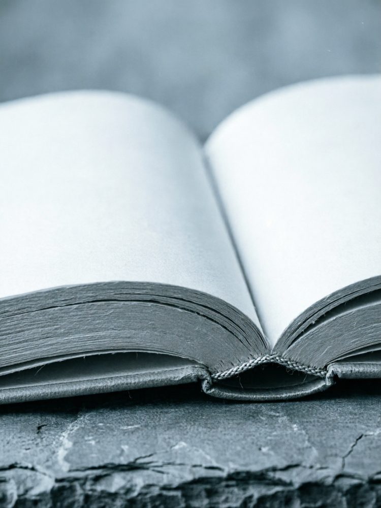 Livro aberto de capa escura com páginas claras sobre uma superfície de pedra cinzenta