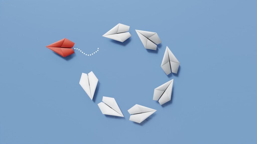 Aviões de papel em circulo com um dos aviões de cor diferente a desviar-se da rota