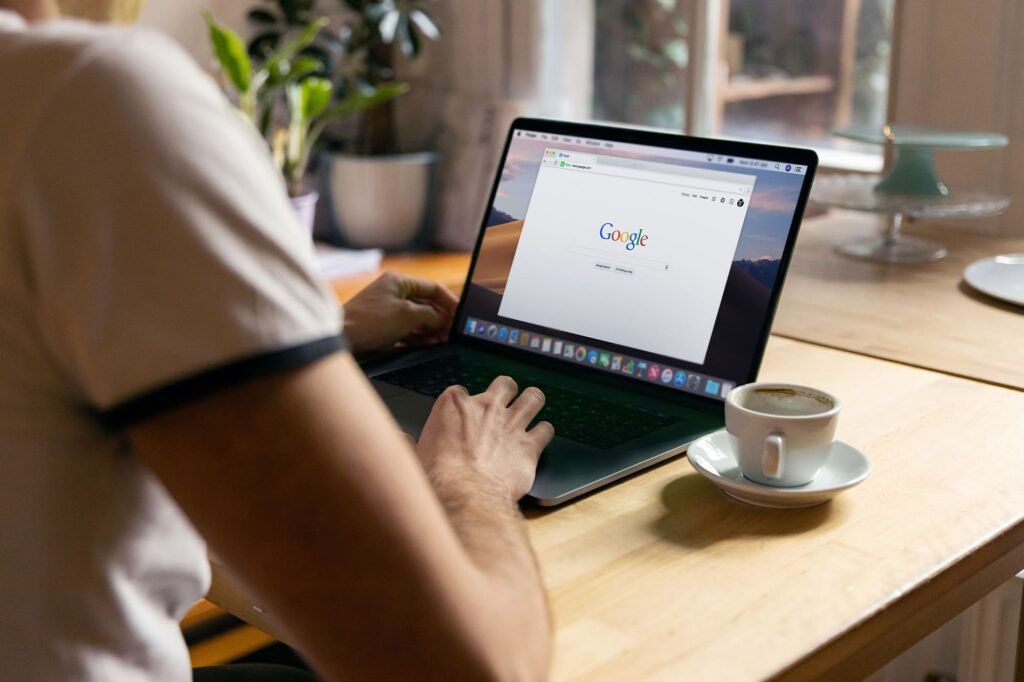 Pessoa a escrever num portátil com a página do Google aberta, ao lado de uma chávena de café