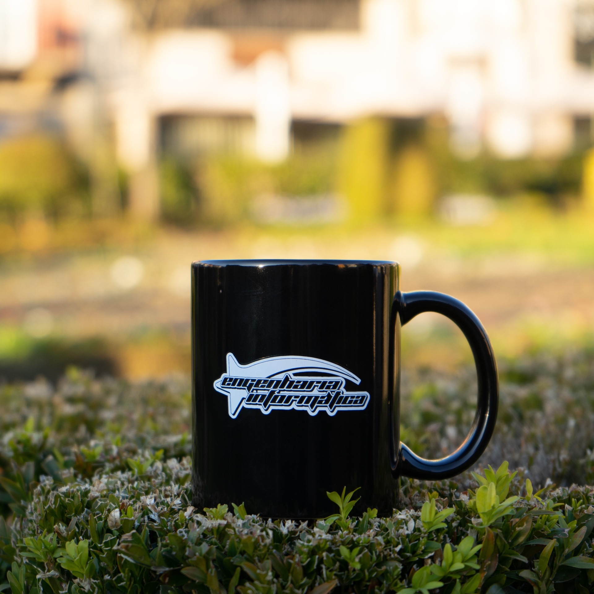 Caneca preta com logótipo branco sobre folhagem verde