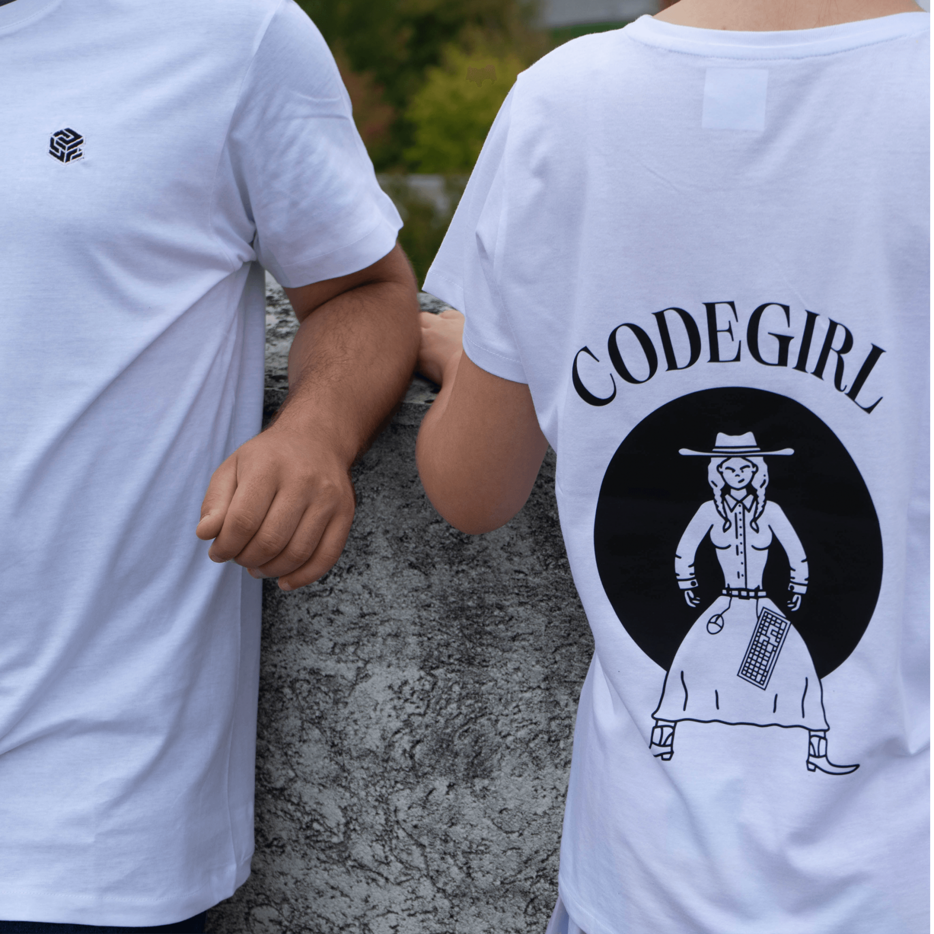 Duas pessoas com t-shirts brancas, uma com logotipo no peito e outra com texto e ilustração nas costas