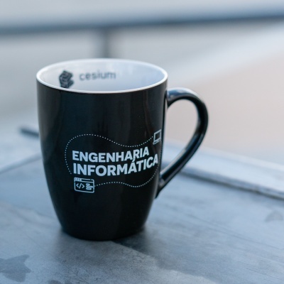 Caneca preta com texto ENGNHARIA INFORMÁTICA em branco numa superfície metálica