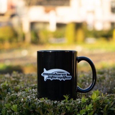 Caneca preta com logótipo branco sobre folhagem verde