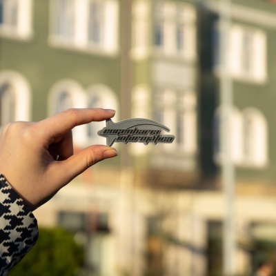 Pessoa a segurar autocolante 'superbong propylan' com casaco pied-de-poule em fundo de edifício