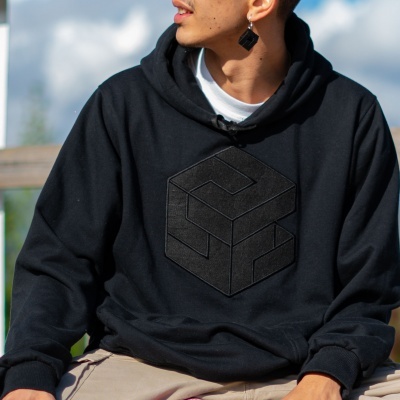 Sweatshirt preta com padrão geométrico tridimensional a preto no peito, usada por pessoa sentado ao ar livre