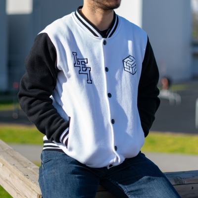 Casaco varsity branco com mangas pretas e bordados pretos sentado ao ar livre.