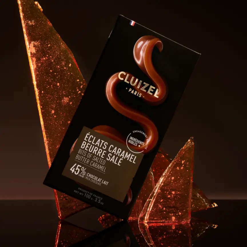 Tablete de Leite com Manteiga Salgada Eclats Caramelo 45% Barra de chocolate Cluizel Paris Éclats Caramel Beurre Salé embalada em fundo escuro com caramelo.