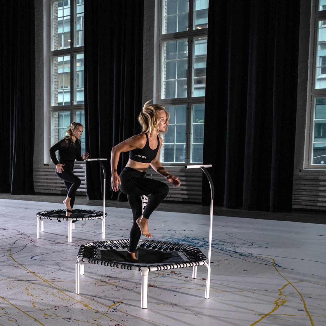 Dois trampolins de fitness pequenos com barras de apoio em interior com grandes janelas