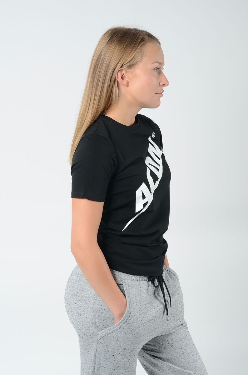 Mulher de perfil com t-shirt preta ADAN e calças de fato de treino cinzentas