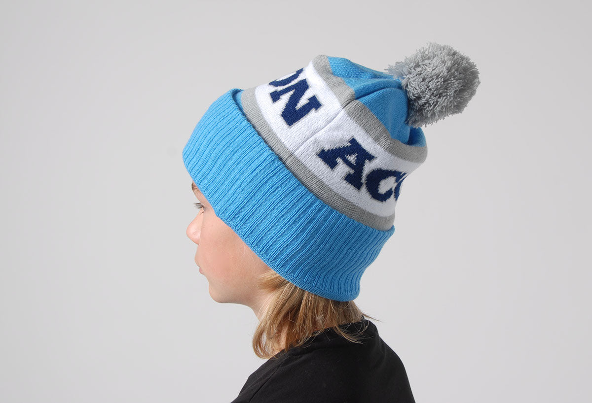 Gorro azul claro com faixa branca e cinzenta e pompom cinzento usado por criança