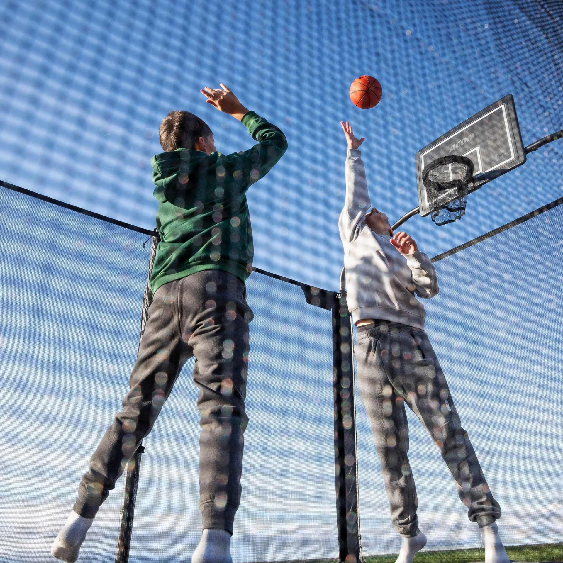 Duas pessoas a jogar basquetebol ao ar livre, vistas através de uma rede.