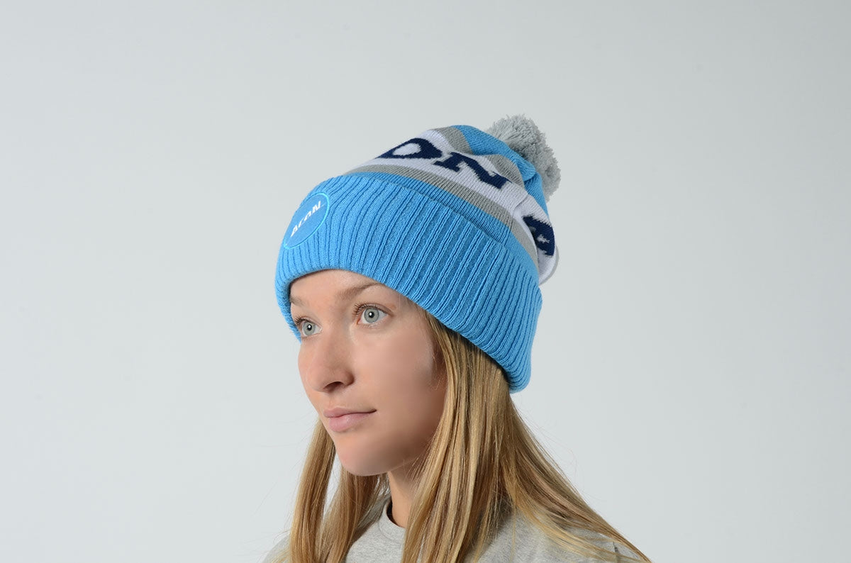 Gorro azul claro com pompom cinzento usado por mulher loira