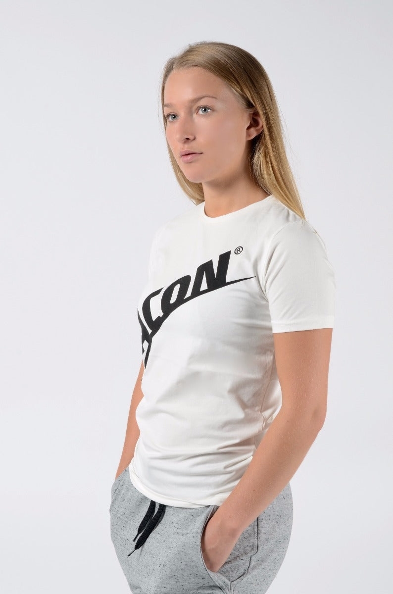Pessoa com t-shirt branca de manga curta com texto preto ICON e calças cinza claro.